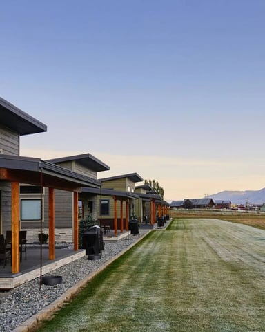 Row of modern cabins with covered porches and a shared lawn, mountains visible in the background at dawn