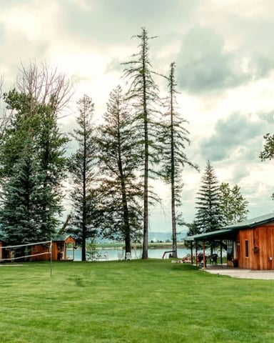 Spacious lawn with volleyball net and cedar outbuildings leading down to a lake in Bigfork, Montana